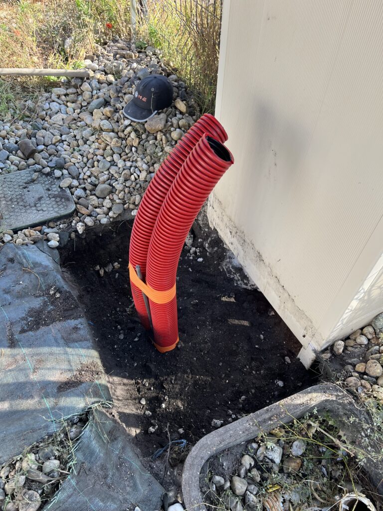 Photo d’une tranchée avec une gaine électrique posée, entourée de sable et d’un grillage avertisseur à Villeneuve-sur-Lot (47300).